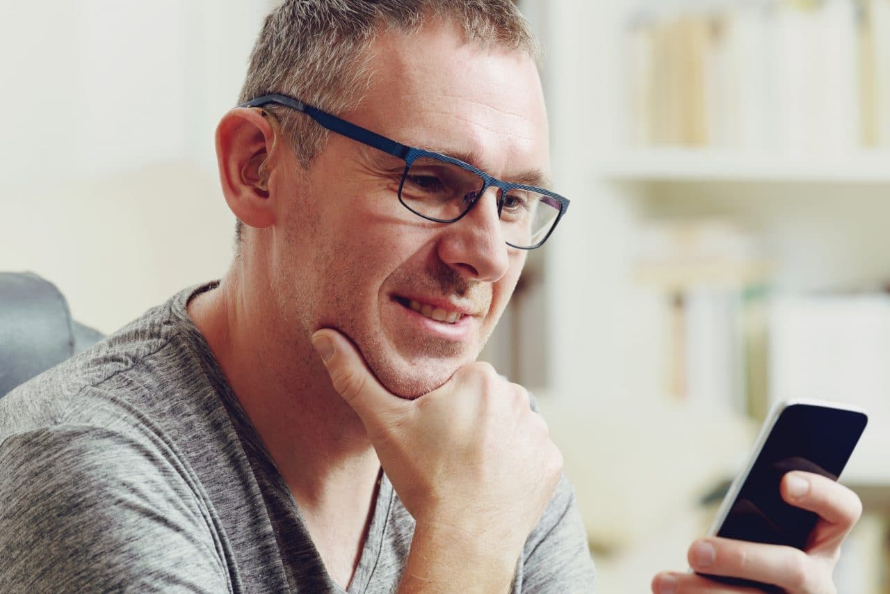 Man with hearing loss and with hearing aid using smart phone at home or at office