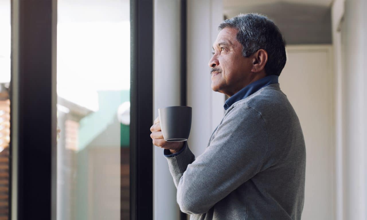 Man drinking coffee and looking thoughtfully out his window.