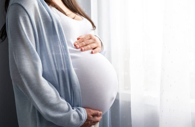 A side view of pregnant woman holding her stomach