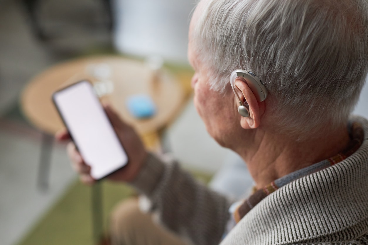 Man with hearing aids looks at phone