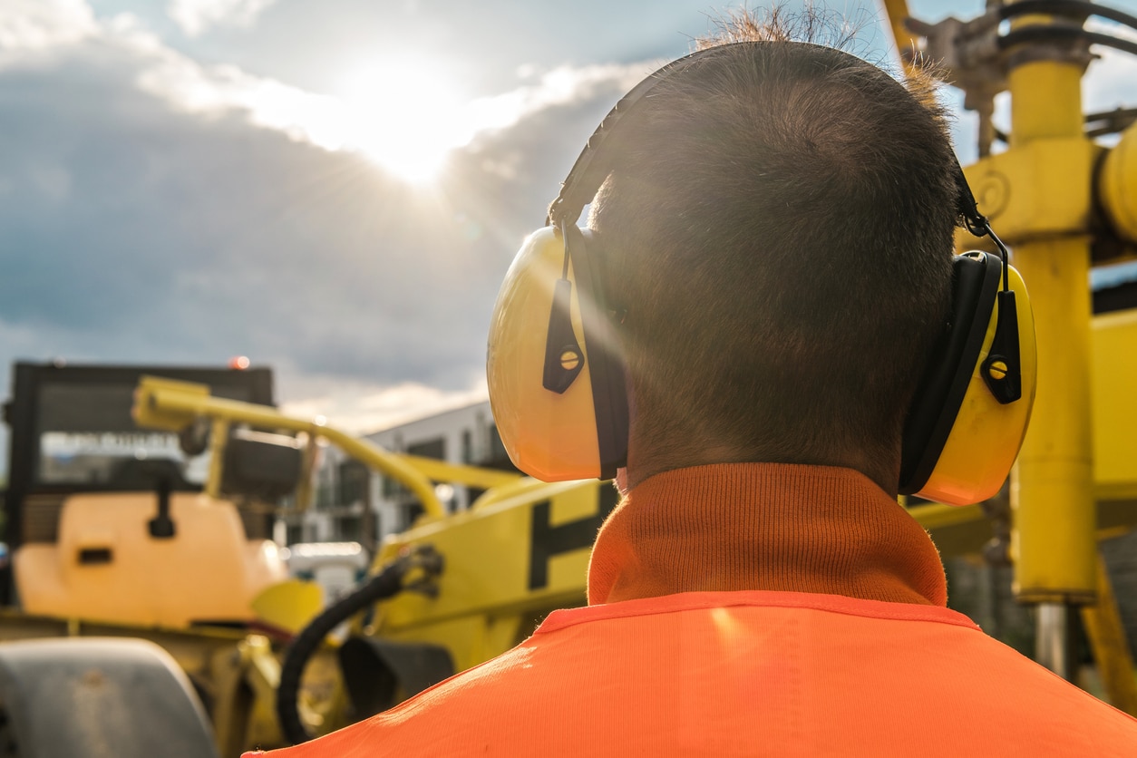 Man wearing earmuffs around construction equipment.