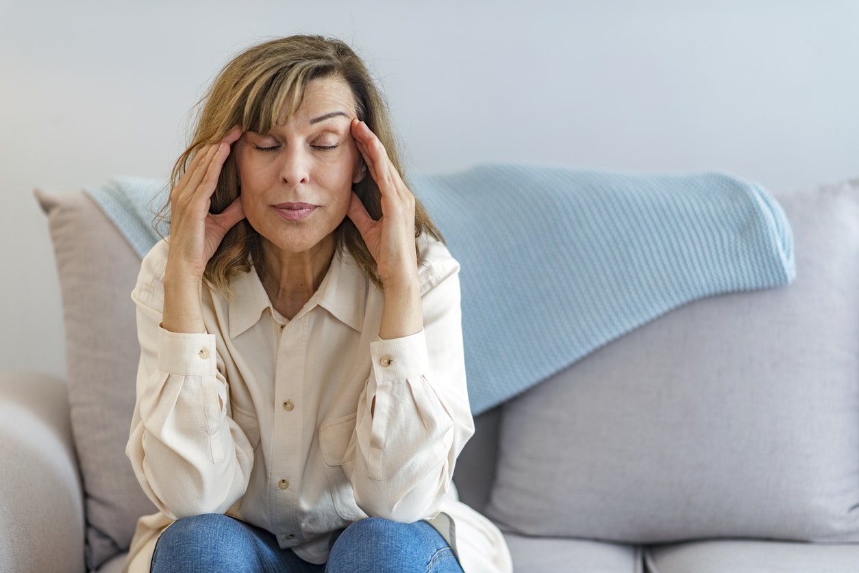 Stressed woman massaging her temples while sitting on a couch